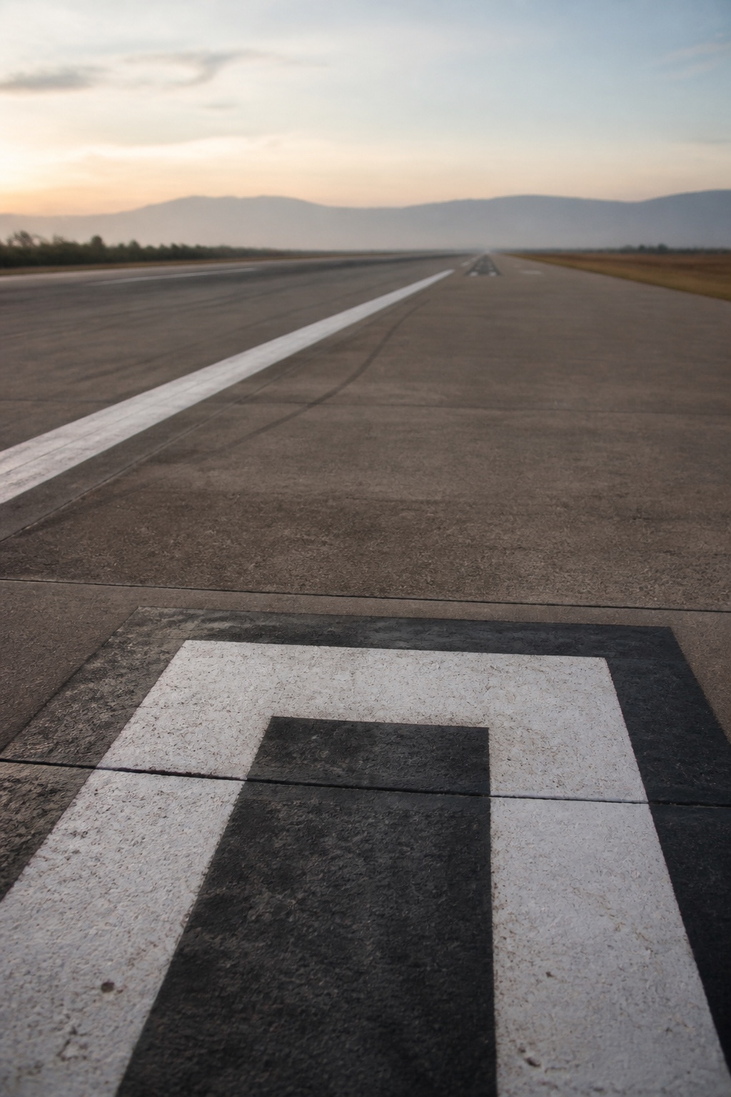 A painted distance marker at the near end of an empty runway in early morning light